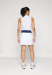 White athletic dress featuring a fitted sleeveless top, navy waistband, and pleated skirt. Smooth texture with a breathable fabric.