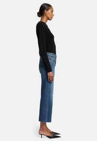 Maglione corto nero, jeans in denim blu a gamba dritta e mule nere a punta, caratterizzati da una texture morbida e linee di design pulite.