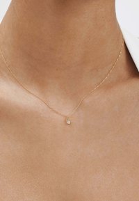 Collar de cadena de oro con un delicado colgante en forma de lágrima que presenta una pequeña gema clara, sobre un fondo de piel suave.
