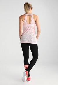 Różowy, teksturowany tank top z wycięciem typu racerback; zestawiony z dopasowanymi czarnymi legginsami z różowymi akcentami i tekstem w stylu pisanym.