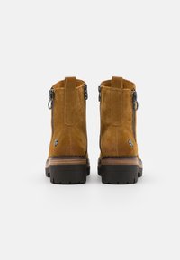 Suede ankle boots in mustard yellow with a rounded toe, side zippers, and a thick black rubber sole with layered brown accents.