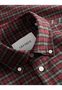 Camicia flanella a quadri rossi e neri con colletto classico, bottoni bianchi e un'etichetta con la scritta "LES DEUX" all'interno del colletto.