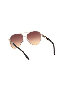 Gafas de sol aviador de metal dorado con lentes marrones degradados. Las varillas de acetato negro presentan un detalle de logo y una textura brillante. Incluyen almohadillas nasales transparentes.