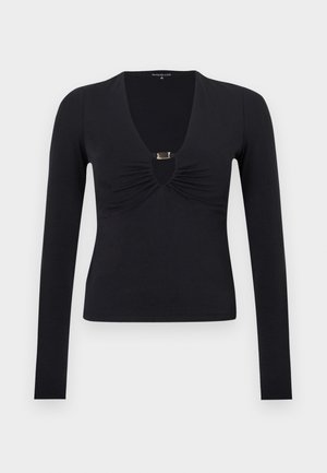 Haut noir à manches longues avec un décolleté en V profond, tissu froncé au niveau de la poitrine, et une découpe avant soulignée par un détail en métal doré.