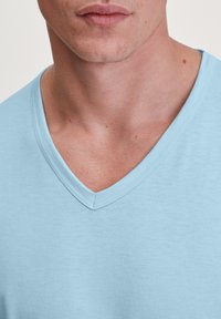 T-shirt en coton bleu clair à col en V, texture lisse, manches courtes, avec un col légèrement côtelé et une coupe décontractée.