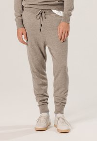 Graue Sweatpants aus weichem Material, mit einem elastischen Bund und Kordelzug, gerippten Bündchen und Seitentaschen. Kombiniert mit weißen Sneakers.