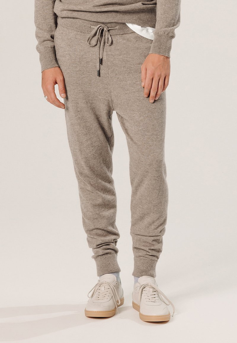 Graue Sweatpants aus weichem Material, mit einem elastischen Bund und Kordelzug, gerippten Bündchen und Seitentaschen. Kombiniert mit weißen Sneakers.