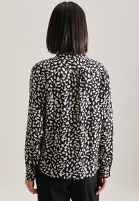 Camicia nera con un motivo astratto bianco, colletto, maniche lunghe e dettagli con piega sul retro. Tessuto liscio e vestibilità comoda.