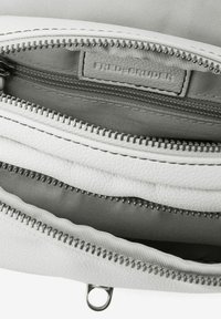 Interior de un bolso de cuero blanco que muestra múltiples compartimentos con cremallera en tela gris; decorado con cremalleras de plata y una etiqueta de la marca.