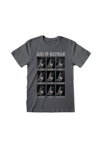 Grijze katoenen T-shirt met acht Batman-gezichten die verschillende stemmingen tonen. Vetgedrukte tekst hierboven luidt "De vele stemmingen van Batman."