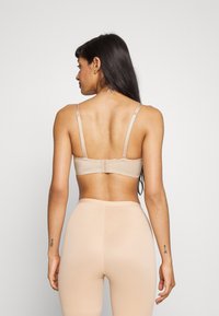 Beige bh med justerbare stropper, mykt stoff og knappelukking. Kombinert med matchende beige leggings med en glattere overflate.