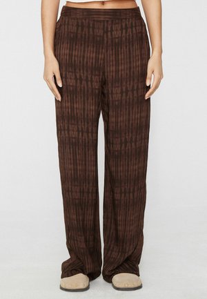 Pantalon marron à jambes larges avec un motif fin de rayures verticales porté par une personne debout, associé à des chaussures beige sans lacets.