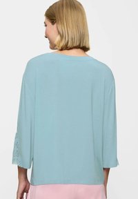 Jasnoniebieska bluzka z długim rękawem z koronkowymi akcentami przy mankietach. Miękka tkanina, luźny krój i okrągły dekolt.