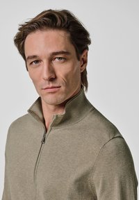 Beżowy sweter rozpinany na zamek z wysokim kołnierzem, wykonany z miękkiej dzianiny, o gładkiej fakturze i subtelnych detalach szwów.