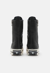 Černé kožené kotníkové boty s uzávěrem na zip, plochou gumovou podrážkou a bílým logem na patě. Hladká textura a elegantní design.