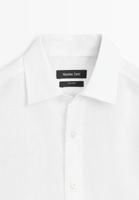 Chemise blanche en lin à boutons avec col pointu, affichant les étiquettes noires "Massimo Dutti" et "100 % lin" à l'intérieur du col.