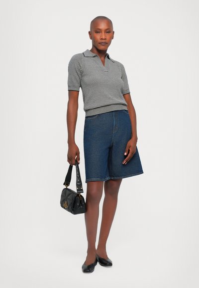 Striped short-sleeve polo shirt in black and white, paired with dark blue denim shorts. Holds a black handbag, wearing black flats.