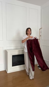 burgundy fluwelen broek met een gladde textuur, volledige lengte, en klassieke tailleband, vastgehouden door een persoon in een witte top en beige broek.
