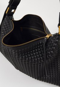 Borsa a tracolla in pelle nera con texture a piramide trapuntata, chiusura zippata in oro e tasche interne. La tracolla comprende accenti dorati per un tocco di stile.