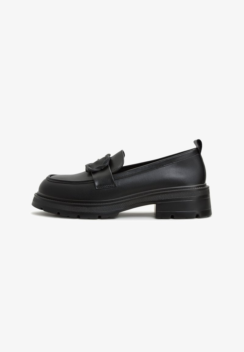 Mocassin en cuir noir avec semelle épaisse et détail de nœud décoratif sur le dessus, vue de profil sur fond blanc.