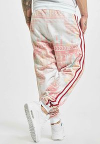 Pink and white joggers with geometric patterns, red side stripes, and a tapered fit, paired with white sneakers. Smooth texture.