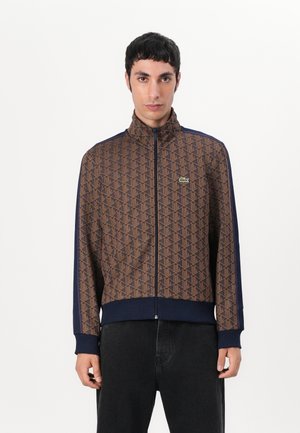 Brown patterned zip-up jacket with navy accents, high collar, ribbed cuffs, and a small logo. The fabric has a smooth texture.