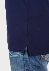 Navy blue cotton T-shirt with side slits at the hem, paired with light blue denim jeans featuring orange stitching and faded texture.