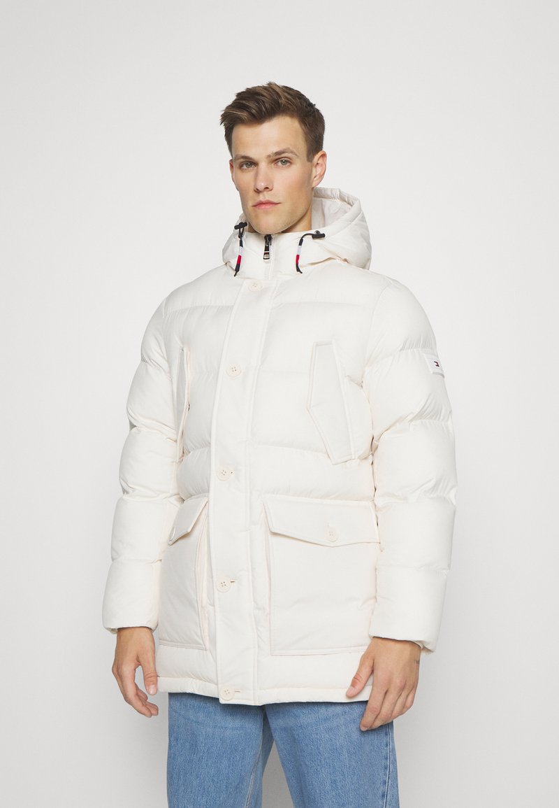 Chaqueta acolchada de crema clara con capucha, cierre de botones en el frente, dos bolsillos frontales y cordones elásticos. Tejido texturizado y acolchado.