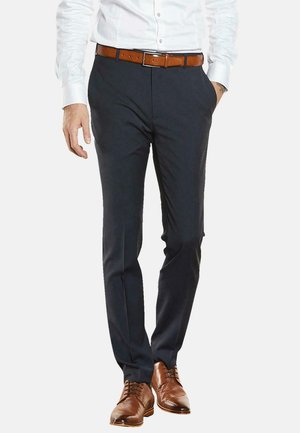 Navyfarbene Anzughose mit schlanker Passform, seitlichen Taschen und einer glatten Textur. Kombiniert mit einem weißen Hemd und braunen Lederschuhen.
