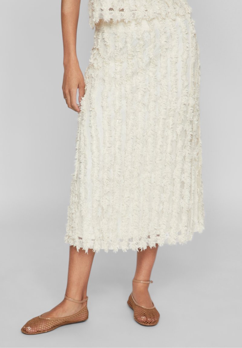 Valkoinen midi-hame, jossa on teksturoitu, fringitettävä muotoilu ja suora leikkaus. Yhdistetty kevyisiin ruskeisiin, rei'itettyihin tasapohjaisiin kenkiin, joissa on nilkkahihnat.