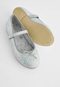 Bailarinas plateadas con un upper texturizado cubierto de rhinestones. Presentan un acento de lazo y un interior suave y acolchado para mayor comodidad.