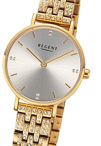 Montre en métal doré avec un cadran argenté, présentant un design minimaliste, des accents en cristal et un bracelet à motifs. Nom de la marque "REGENT" affiché.
