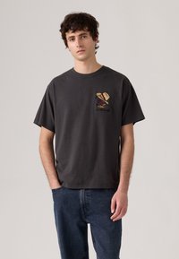 Camiseta de algodón gris oscuro con mangas cortas, escote redondo y diseño bordado en el lado izquierdo del pecho que presenta un sombrero y adornos.