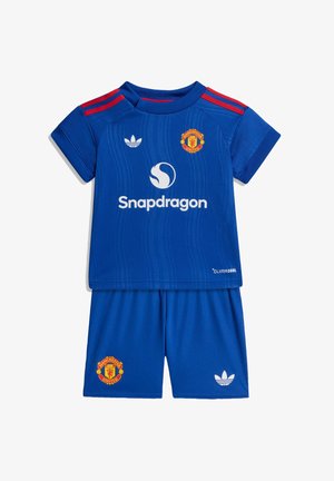 Niebieski strój piłkarski Manchester United dla dzieci z czerwonymi paskami na ramionach, logo Snapdragon, logotypami Adidas oraz herbami drużyny na koszulce i spodenkach.