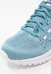 Světle modrá sportovní obuv vyrobená z prodyšné síťoviny, s texturovaným svrškem, bílými akcenty a polstrovanou podrážkou se zřetelným vzorem. 