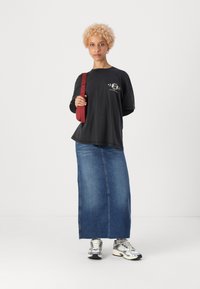 Fekete, oversized, hosszú ujjú póló grafikus nyomattal, kék farmer maxiszoknyával párosítva. Piros vállpánt és ezüst sportcipő.