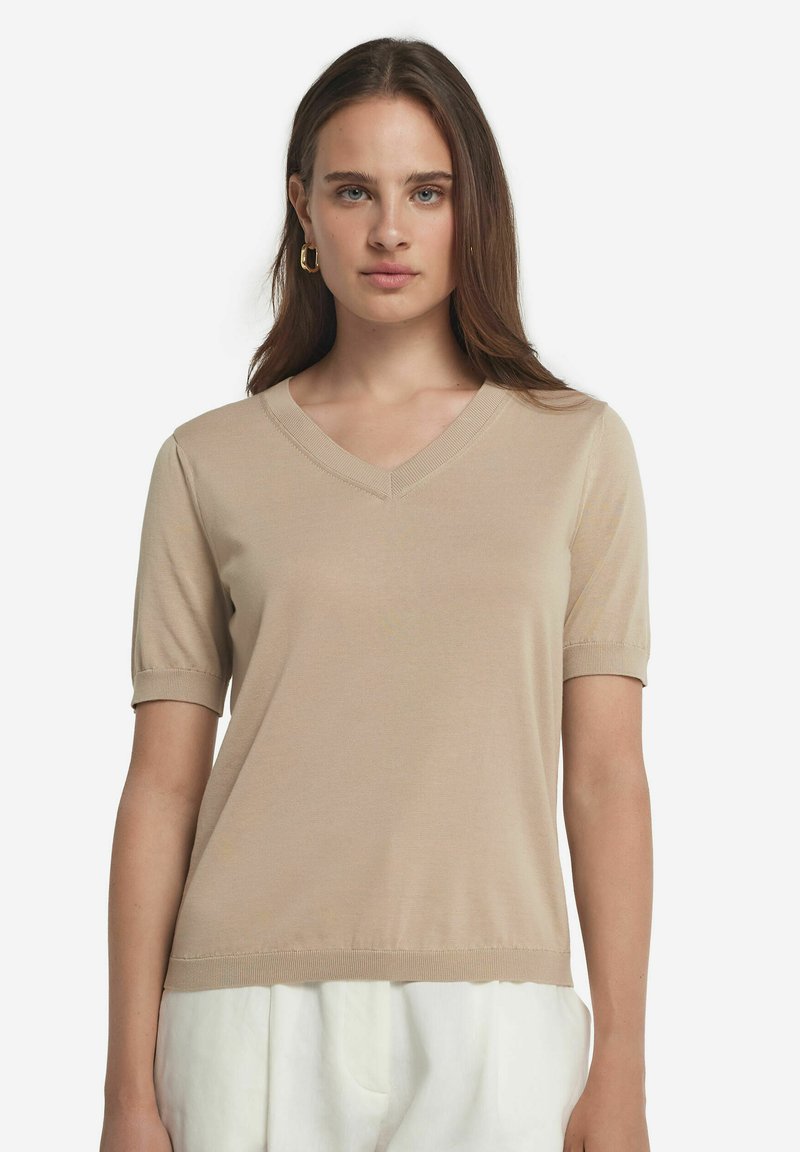 Beige kortærmet strik toppen med V-hals og ribbede manchetter og kant, lavet af et glat, letvægtsstof. Enkel design, ingen synlige mønstre eller accenter.