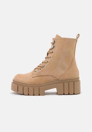 Tan ruskinds ankelstøvler med rund tå, snørebåndsfront, metaløjer og en chunky lagdelt sål for ekstra højde.