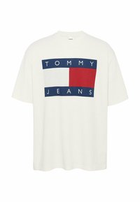 Camiseta de algodón blanca con un logo rectangular en azul y rojo que dice "TOMMY" en la parte superior y "JEANS" en la parte inferior, mangas cortas, ajuste relajado.