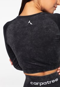 Sort crop top med tekstureret overflade, der har et lille hvidt logo på ryggen og ribbede manchetter. Designet er tætsiddende og atletisk.