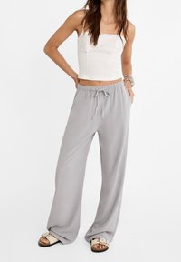 Vaaleanharmaat leveälahkeiset housut, joissa on joustava vyötärö ja naru, yhdistettyinä tiukkaan valkoiseen lyhythihaiseen paita. Pehmeä kangastekstuuri.