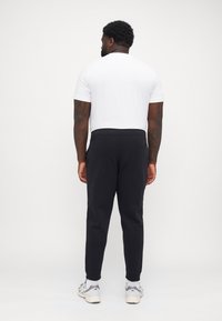 Schwarze Jogginghose aus weichem Stoff, mit einem elastischen Bund und schmal zulaufendem Bein. Kombiniert mit einem schlichten weißen T-Shirt.