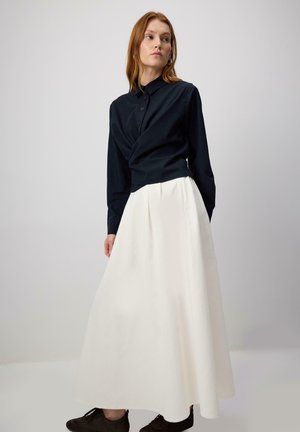 Navy button-up shirt with long sleeves and textured fabric, paired with a flowing white floor-length skirt. Dark shoes complete the outfit.