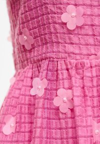Tissu rose texturé à motif quadrillé, décoré de petites applications de fleurs roses translucides cousues sur la surface.