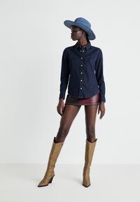 Koszula dżinsowa z guzikami z przodu, długimi rękawami i westernowym fasonem; zestawiona z burgundową mini spódnicą i beżowymi kozakami do kolan.