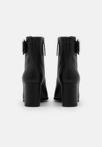 Bottes cheville en cuir noir avec une finition texturée, talons carrés, fermetures éclair latérales et une boucle décorative sur la cheville extérieure.