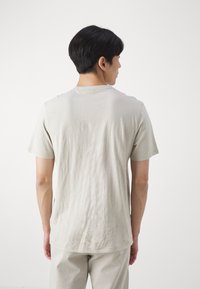 T-shirt beige clair en tissu doux et texturé. Manches courtes, col rond classique, coupe décontractée. Design minimal, sans logos ni motifs visibles.