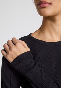Maglia nera a coste con maniche lunghe e scollatura rotonda. Presenta una silhouette aderente e maniche leggermente più lunghe con dettagli di cucitura visibili.