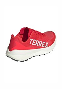 Scarpa sportiva rossa con tomaia in rete traspirante, logo TERREX bianco, intersuola bianca imbottita e suola nera testurizzata per trazione.