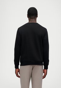 Μαύρη μπλούζα με στρογγυλή λαιμόκοψη και ριγέ μανσέτες, κατασκευασμένη από μαλακό ύφασμα. Λογότυπο 'Karl Lagerfeld' στη λαιμόκοψη στο πίσω μέρος.